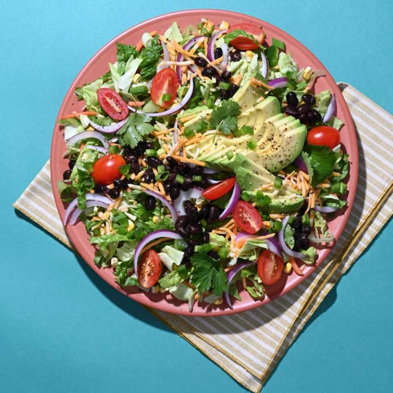 Colorful fiesta taco salad topped with avocado ranch dressing and fresh vegetables.