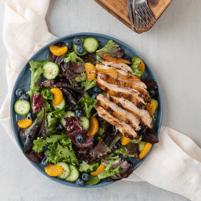 Fresh and fruity spring mix salad topped with grilled chicken thighs, ideal for a healthy meal option.