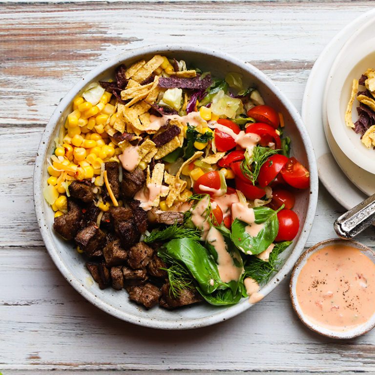 Steak taco salad with fresh vegetables, cheese, and avocado served in a bowl, garnished with cilantro.