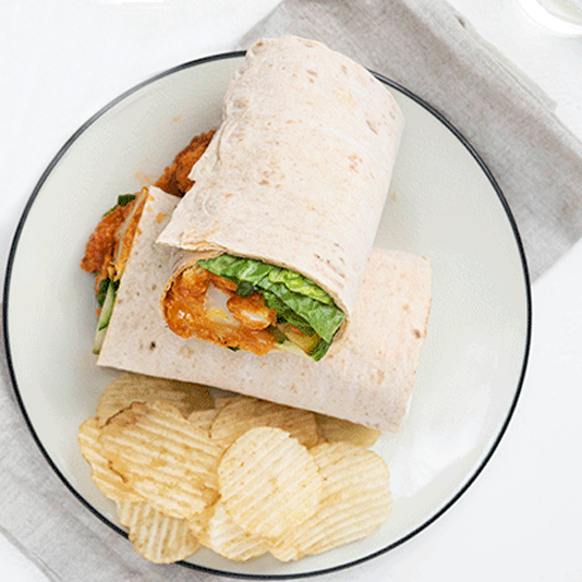 Buffalo cauliflower and kale wraps on a wooden board, garnished with fresh vegetables.