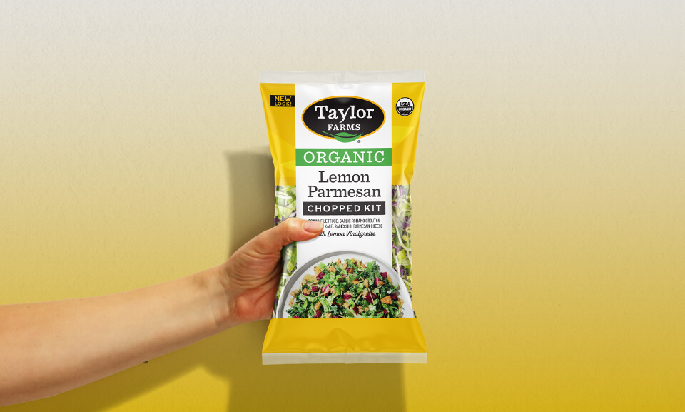 Hand holding a bag of Taylor Farms Organic Lemon Parmesan salad mix.