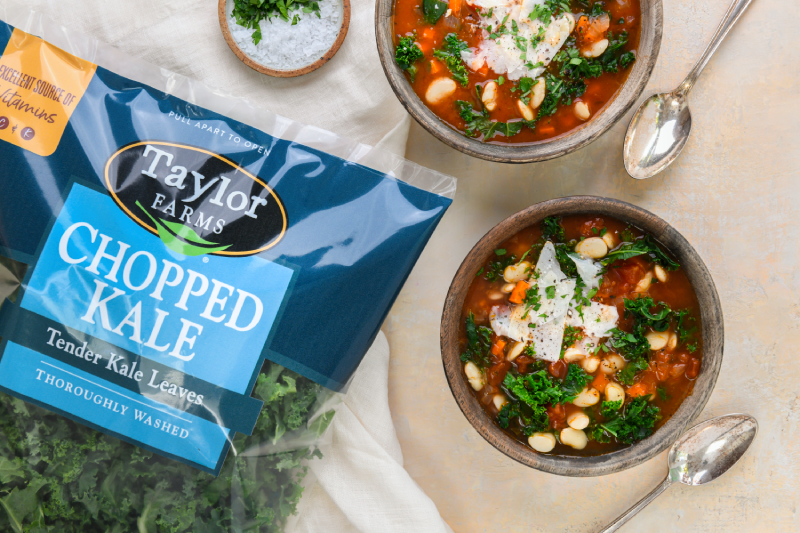 Bag of Taylor Farms chopped kale next to two bowls of soup