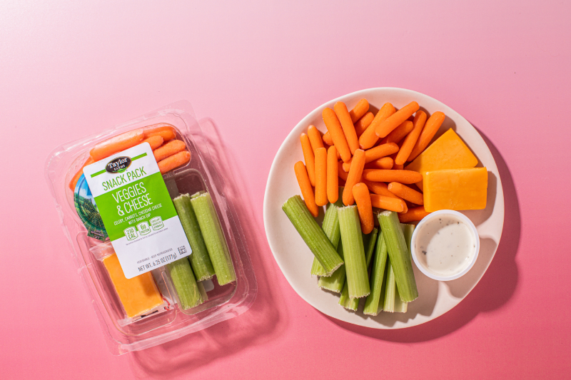 Taylor Farms Snack Pack of Veggies & Cheese in a package and laid out on a plate on a pink background