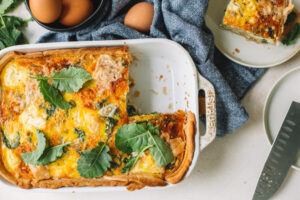 Taylor Farms Sausage, Kale, and Ricotta Quiche in a dish on a table next to eggs and plates