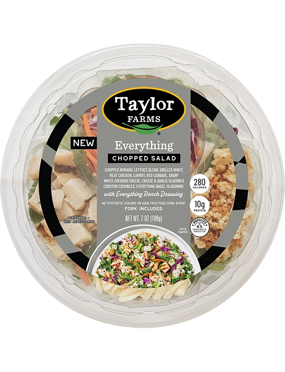 The Taylor Farms Everything Chopped Salad Bowl package, showing chopped romaine lettuce, grilled white meat chicken, carrot, red cabbage, sharp white cheddar cheese, cheese & garlic seasoned crouton crumbles, everything bagel seasoning, and everything ranch dressing.