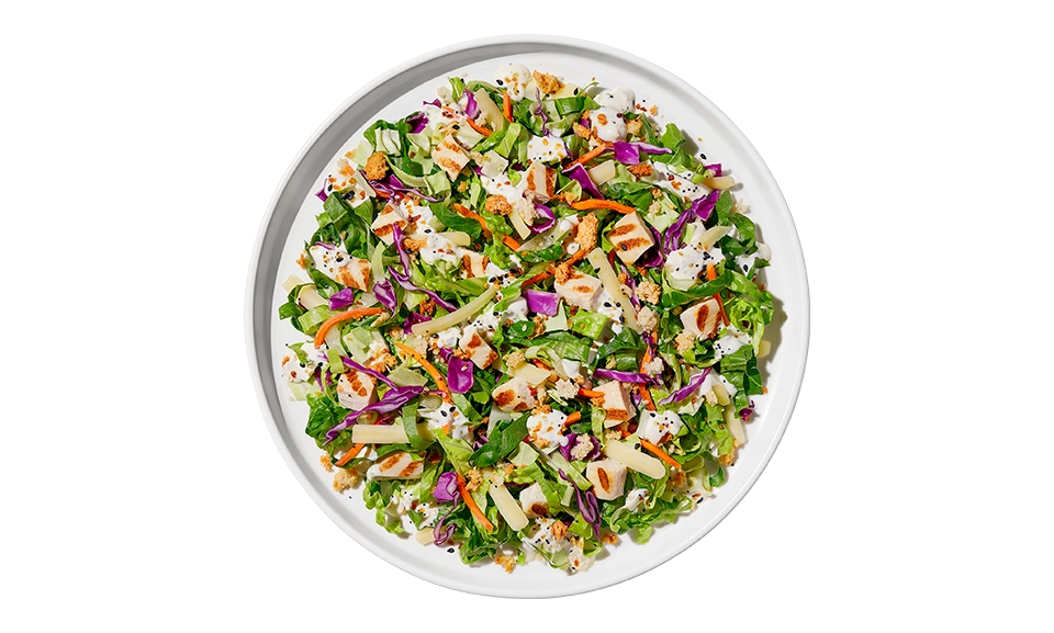 The Taylor Farms Everything Chopped Salad Bowl package, showing chopped romaine lettuce, grilled white meat chicken, carrot, red cabbage, sharp white cheddar cheese, cheese & garlic seasoned crouton crumbles, everything bagel seasoning, and everything ranch dressing.